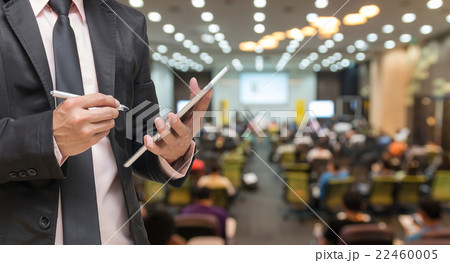 Businessman using the tablet on the Abstract blurred photo of conference hall or seminar room with attendee background Businessman using the tablet on the Abstract blurred photo of conference hall or seminar room with attendee background 22460005