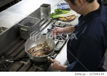 煮汁をかけながら魚を煮る調理師 22506130