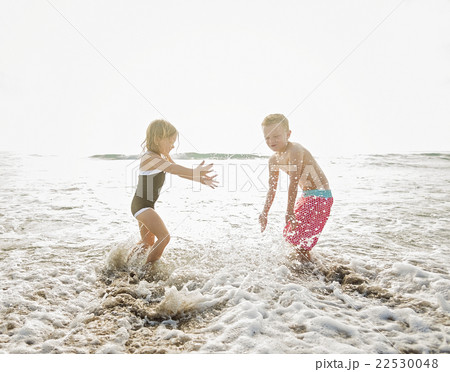 Mother walking with boy (6-7) and girl (4-5) on beach by water 22530048