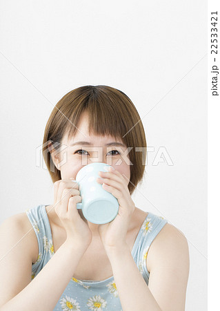 女性 コップ 飲む ショート ボブ 夏服 ワンピース 室内 白バック カメラ目線 笑顔の写真素材