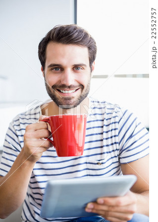 Portrait of happy man holding digital tablet while having cup of 22552757