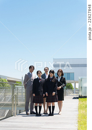 学校をバックに並ぶ講師と女子高校生 22627848