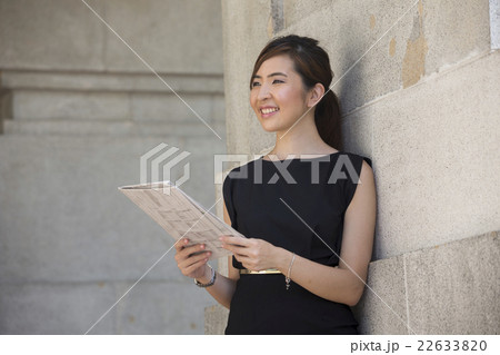 Chinese business woman reading a newspaper outside an office bui Chinese business woman reading a newspaper outside an office bui 22633820
