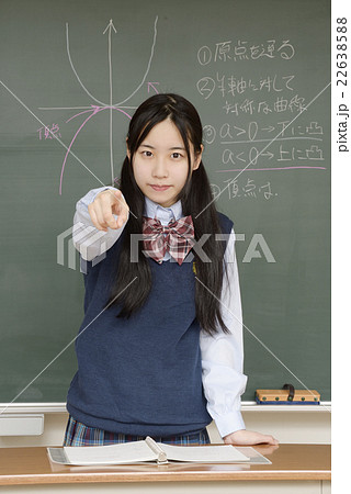 真剣な顔で指さす黒板の前に立つ女子高校生の写真素材