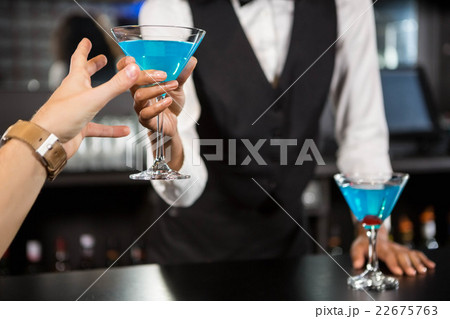 Bartender serving blue cocktail at bar counter Bartender serving blue cocktail at bar counter 22675763