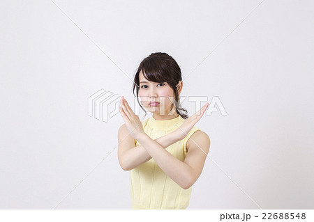 白い背景の前でふくれっ面でばつ印を作る若い女性 22688548