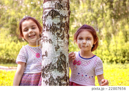 Two young girls stands near a tree 22807656