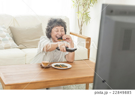 テレビを見ながらお菓子を食べる女性の写真素材