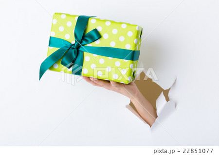 Hand through the hole in paper with present box Hand through the hole in paper with present box 22851077