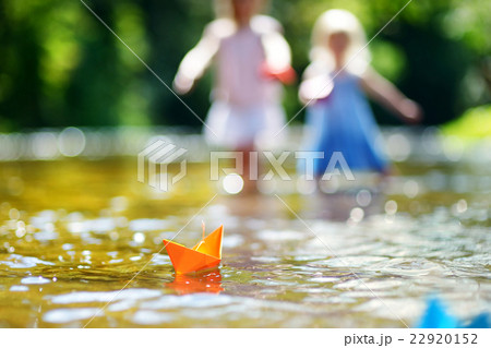 Two sisters playing with paper boats by a river Two sisters playing with paper boats by a river 22920152