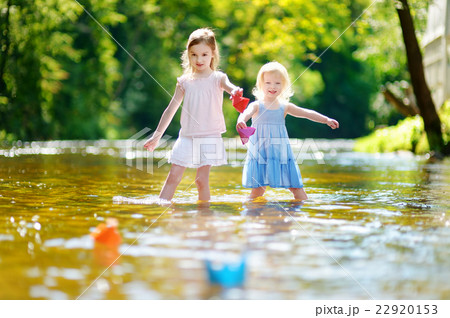 Two sisters playing with paper boats by a river Two sisters playing with paper boats by a river 22920153