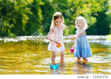 Two sisters playing with paper boats by a river Two sisters playing with paper boats by a river 22920154