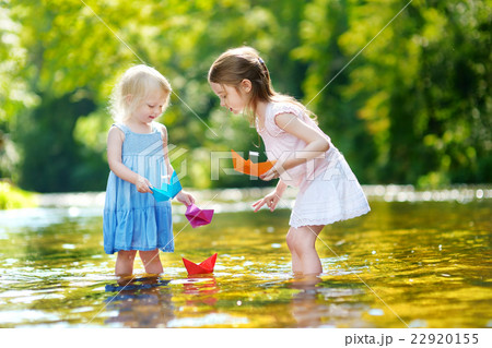 Two sisters playing with paper boats by a river 22920155