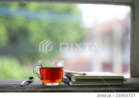 tea in glass and notebook with pencil at windows 23003727