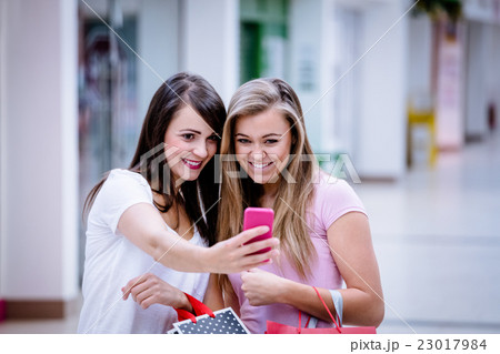 Two beautiful women taking a selfie in shopping mall Two beautiful women taking a selfie in shopping mall 23017984