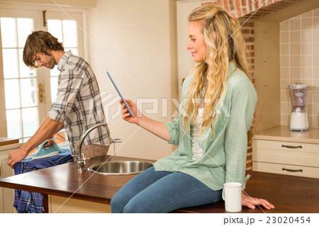 Pretty blonde using tablet while boyfriend ironing a shirt Pretty blonde using tablet while boyfriend ironing a shirt 23020454