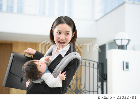 マイホームの前で赤ちゃんを抱っこしているビジネススーツのお母さん 23032781