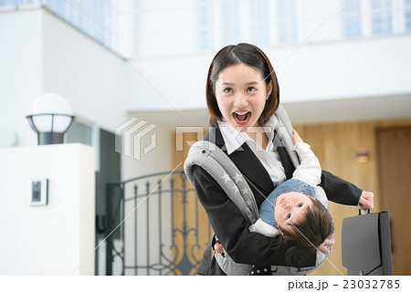 マイホームの前で赤ちゃんを抱っこしているビジネススーツのお母さん 23032785