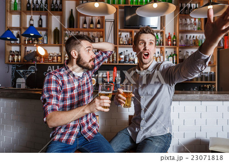 Young people with beer watching football in a bar 23071818