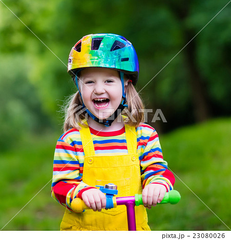 Little girl riding a colorful scooter Little girl riding a colorful scooter 23080026
