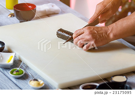 Hand with knife cuts sushi. Hand with knife cuts sushi. 23175095