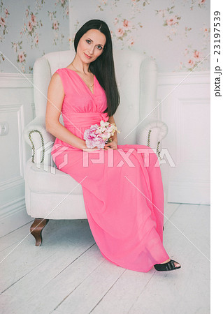 Brunette girl in pink dress sitting white armchair 23197539