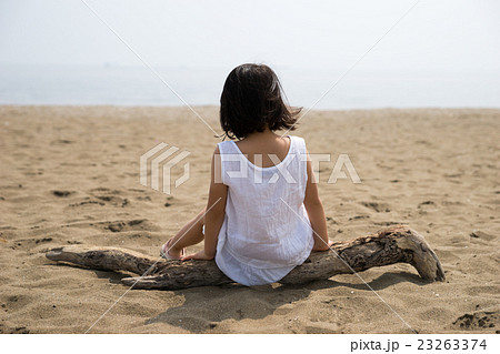 ビーチで流木に座る小さな女の子の写真素材