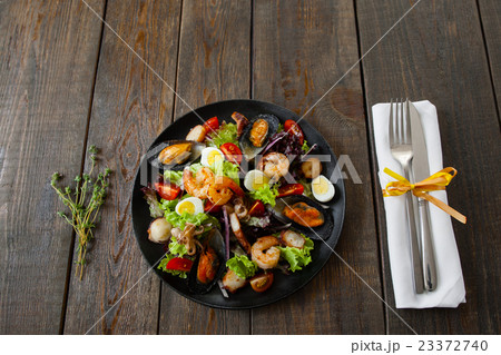 Portion of seafood salad with cutlery on wood 23372740