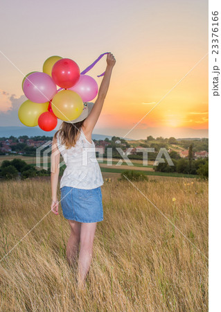 Young woman holding balloons looking at sunset Young woman holding balloons looking at sunset 23376166
