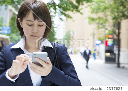 ビジネスウーマン　スマホ　操作　笑み　外　緑　丸の内　通り 23376254