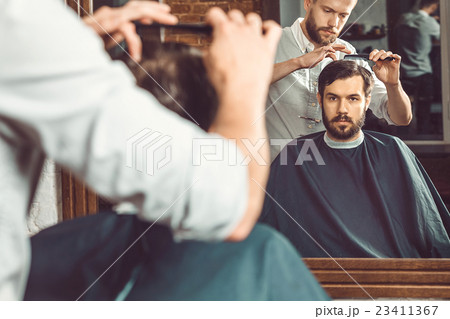 Young handsome barber making haircut of attractive Young handsome barber making haircut of attractive 23411367