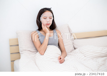 Asian Woman sitting on bed and using the facial mask Asian Woman sitting on bed and using the facial mask 23417410