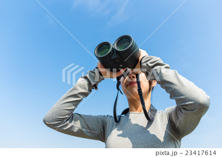 Woman watching though binoculars against the blue sky 23417614