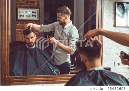 Young handsome barber making haircut of attractive 23432603