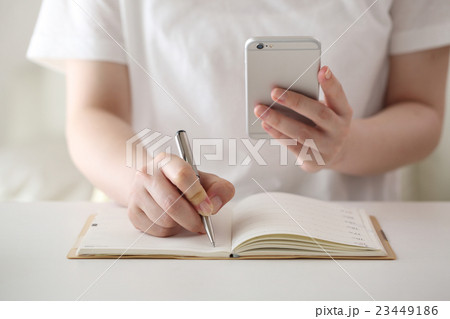 スマホを見ながらメモをする女性 スマホを見ながらメモをする女性 23449186