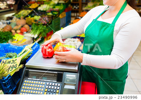 Saleswoman weighting vegetables on scale in grocer 23490996