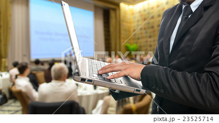 Businessman using the laptop on the Abstract blurred photo of conference hall or seminar room with attendee background Businessman using the laptop on the Abstract blurred photo of conference hall or seminar room with attendee background 23525714