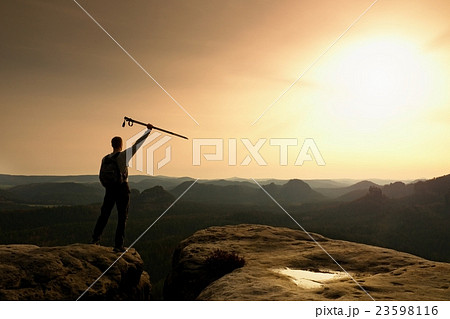 Tourist with poles in hands stand on rock watching 23598116