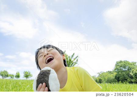 新緑の公園でおにぎりを持って笑う男の子 23620504