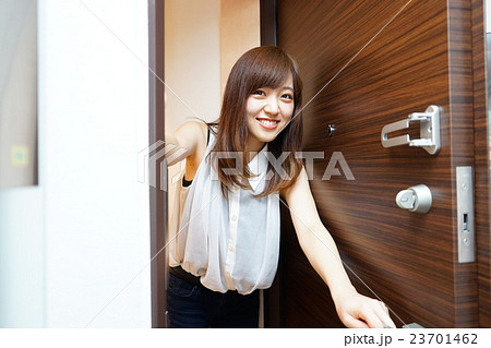 一人暮らしの自宅玄関のドアを開ける若い女性の写真素材