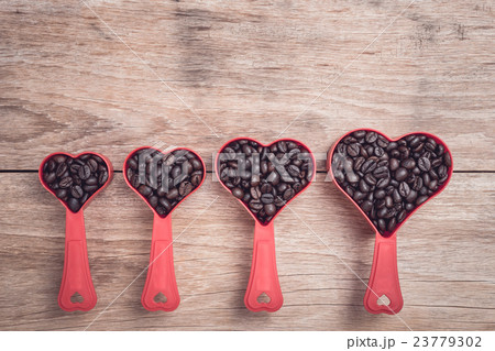 Coffee beans in red heart plastic cup on wooden table top view Coffee beans in red heart plastic cup on wooden table top view 23779302