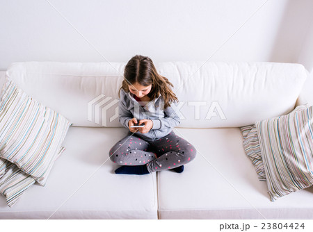 Little girl sitting on sofa, playing with 23804424