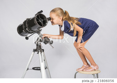 Seven-year girl standing on a chair and looks ridiculous in the eyepiece of the telescope reflector 23806056