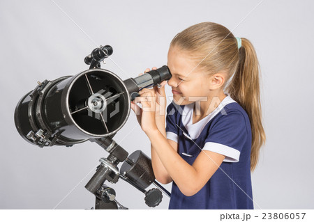 Seven-year girl squinting with interest looks in a reflector telescope 23806057