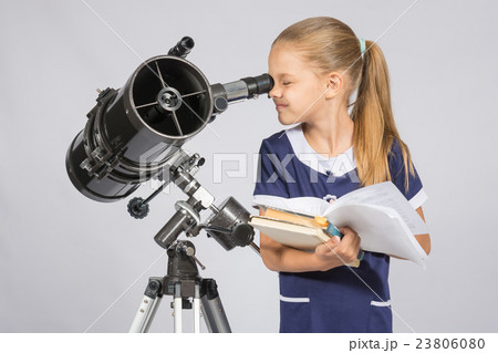 School girl looking through a telescope standing with textbooks 23806080