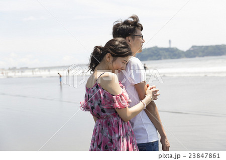 カップル 海 汎用イメージ 海を見つめがら腕を抱く 全身 湘南 江ノ島背景の写真素材