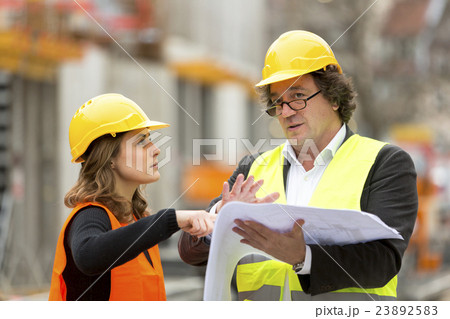 Two engineers, man and woman, reading blueprints 23892583
