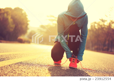 young fitness woman runner tying shoelace on road 23912554