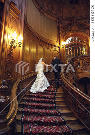 Groom holds bride's hand while going upstairs Groom holds bride's hand while going upstairs 23933426