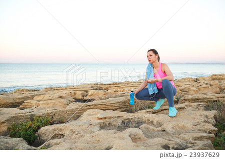 Woman sitting after morning running on the rocks by the sea Woman sitting after morning running on the rocks by the sea 23937629